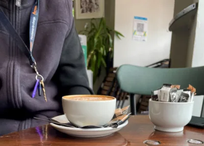 Coffee cup on table, person wearing Action Homeless lanyard
