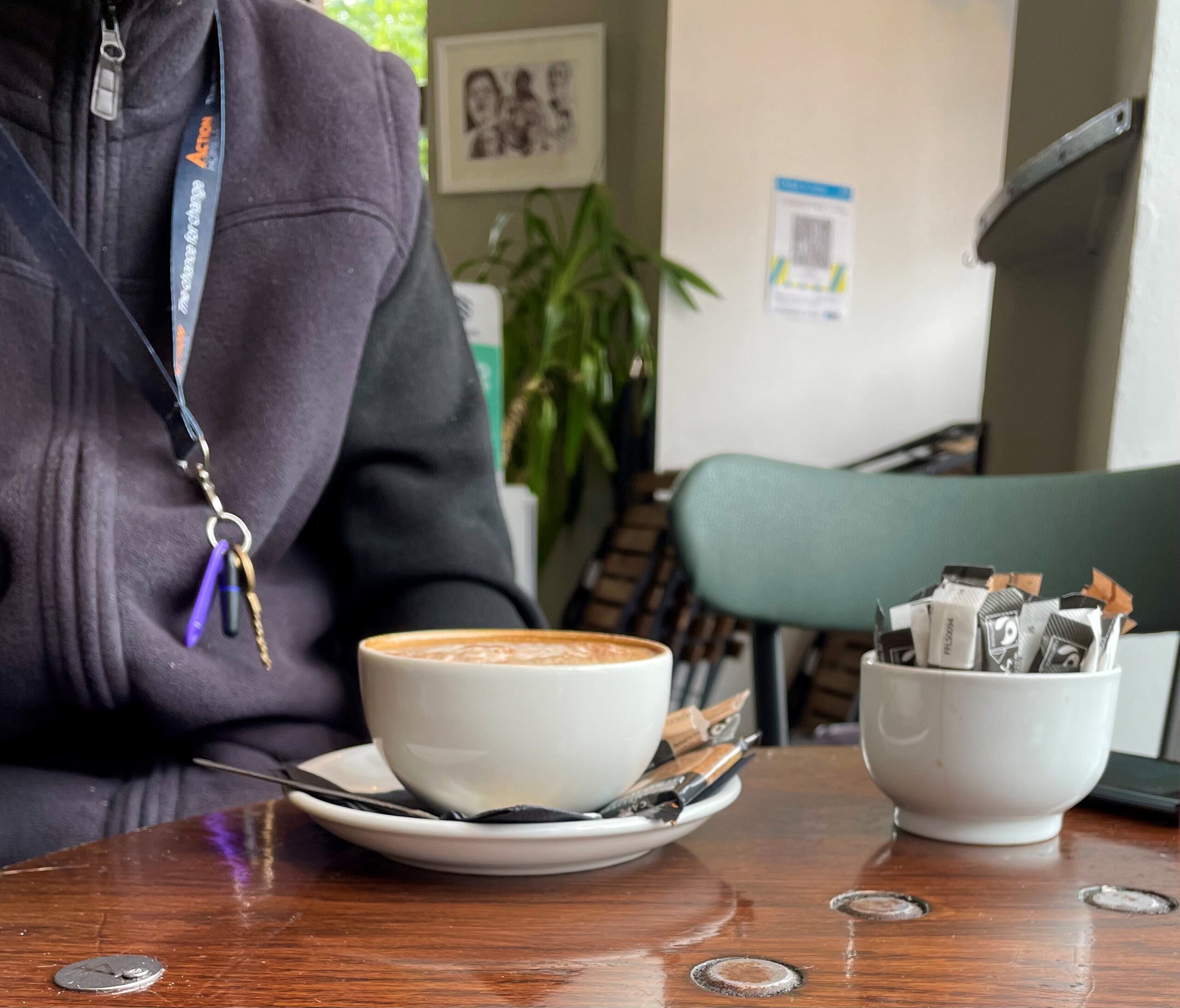 Coffee cup on table, person wearing Action Homeless lanyard